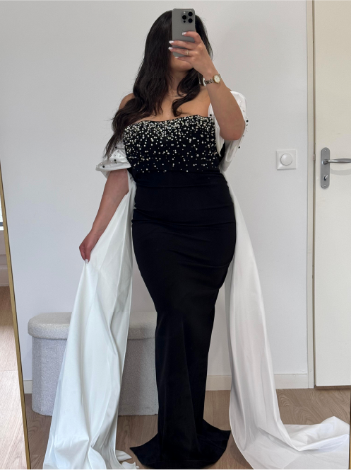 Robe de soirée noire ajustée avec bustier perlé et cape blanche, style chic et raffiné.